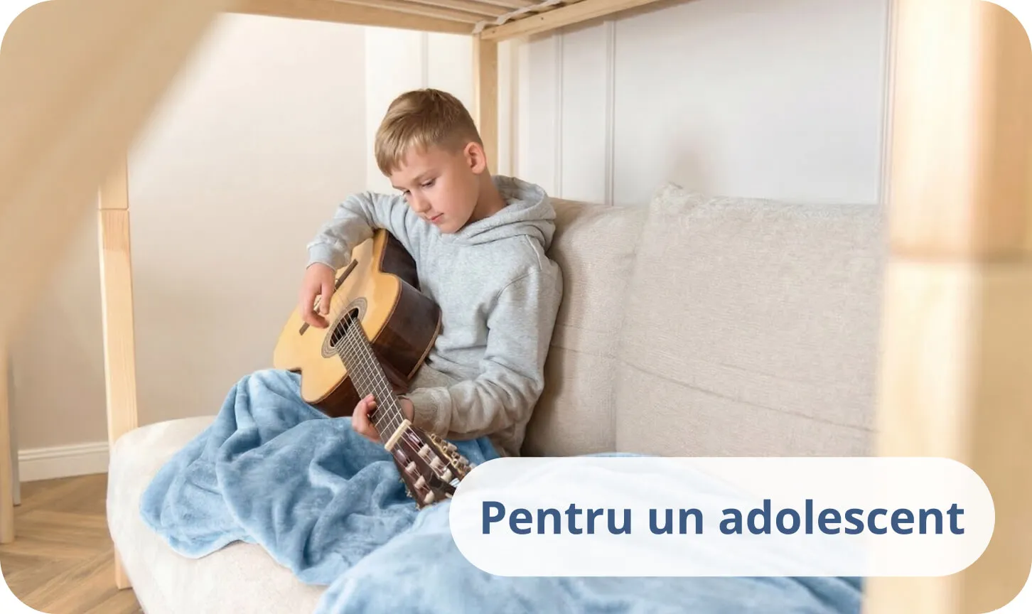 Adolescent cântând la chitară acustică pe un pat acoperit cu o pătură albastră.